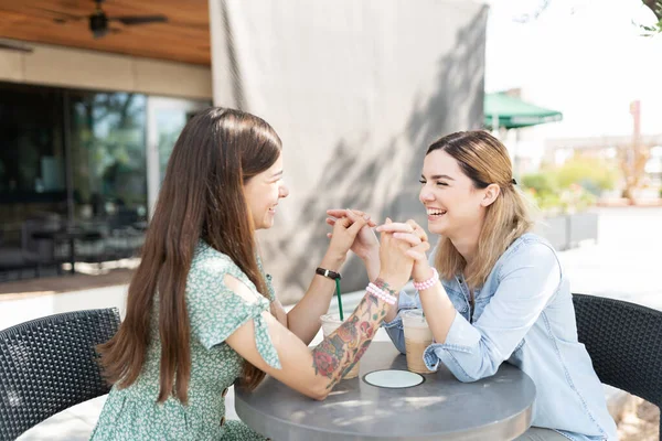魅力的なレズビアンガールフレンド笑っている間に彼らの手を取り合ってテーブルの上にコーヒーショップの外 — ストック写真