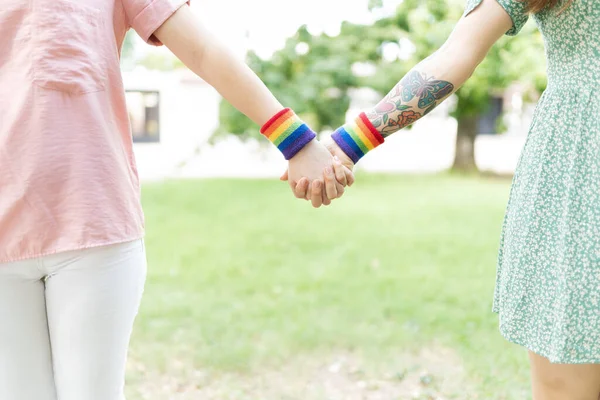 閉じるアップの二つのレズビアンガールフレンド保持手と身に着けている虹旗リストバンド — ストック写真