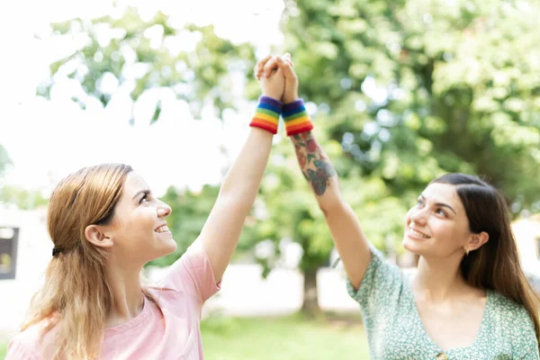 魅力的な若い女性の友人のペアは 空気中で彼らの手とLgbtの虹色のリストバンドを身に着けている — ストック写真