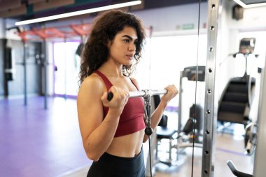 Spor salonunda kablo makinesiyle uyuyan güzel Latin bir kadının yan görüntüsü.