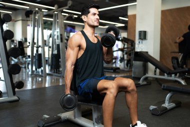 Yakışıklı Latin genç adam iki ağırlık kaldırıyor ve spor salonunda kaslarını kasıyor. 