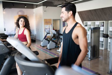 Yakışıklı İspanyol genç adam ve Latin kadın spor salonunda koşu bandında yürürken gülüp eğleniyorlar.