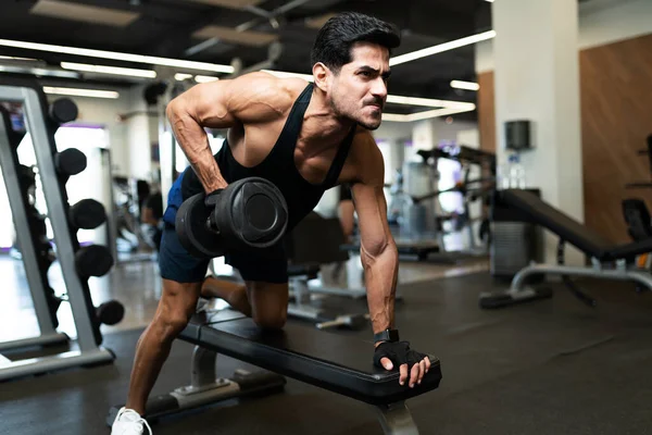 Strong hispanic young man doing a weight lifting workout in a bench at the fitness club