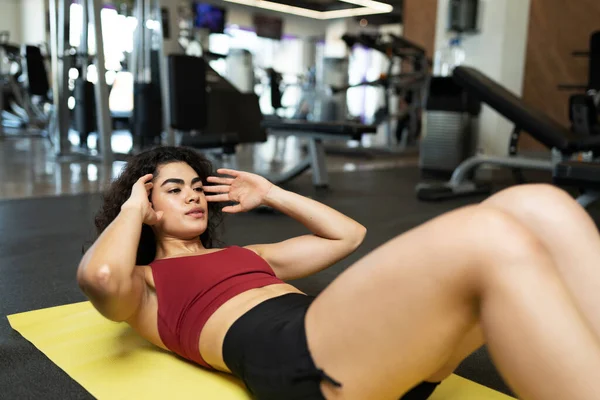 瘦小的年轻女子在体育馆地板的垫子上锻炼腹部和核心肌肉 — 图库照片