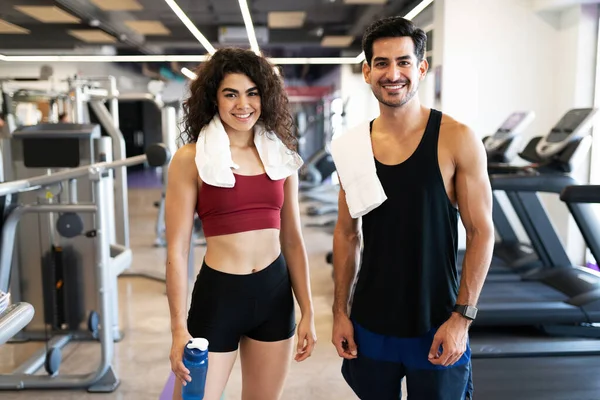 Good looking hispanic young woman and latin young guy smiling and looking happy in the gym