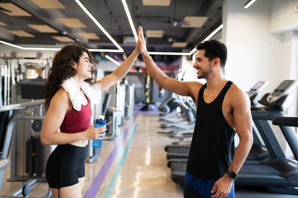 Latin young woman and hispanic fit man laughing and celebrating reaching their fitness goals at the gym