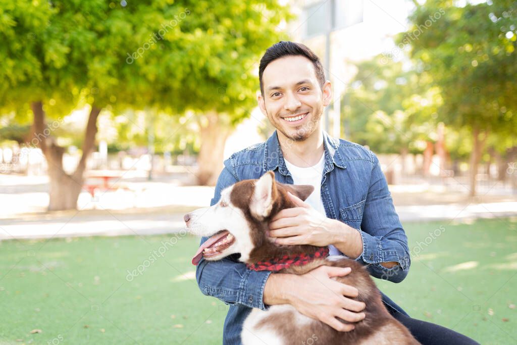 Portrait of an attractive adult man in his 30s giving a hug to a furry dog in the park
