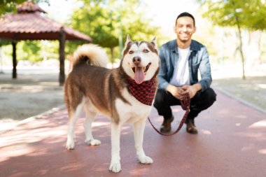 Parkta tasmalı güzel bir köpeğin portresi mutlu erkek sahibinin önünde duruyor ve gülümsüyor. 