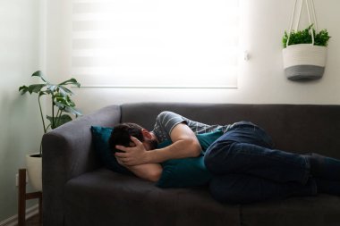 30 'lu yaşlarda erkek, kanepeye kıvrılmış ellerini yüzüne koyup ağlıyor. 