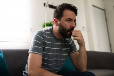 Hispanic man sitting on the sofa and biting his nails, looking anxious and stressed 