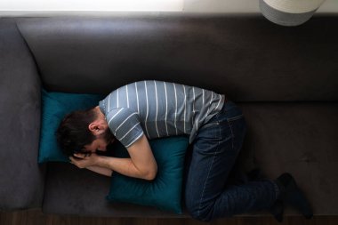 Kanepesine kıvrılmış ağlayan, üzgün ve mutsuz görünen yetişkin bir adamın en iyi görüntüsü.