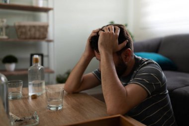 Depresyon ve alkolizm geçiren yetişkin bir adam kafasını kahve masasında içki ve bir şişe votka alkolle tutuyor. 