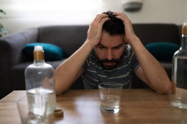 Masasında iki şişe votkayla içkisine dik dik bakan 30 'lu yaşlardaki Latin bir adam.