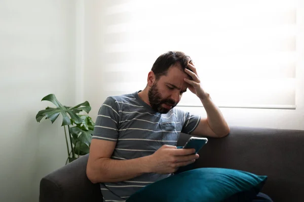 Hispanic Man Sitting Sofa Looking Anxious Preoccupied While Texting His — ストック写真