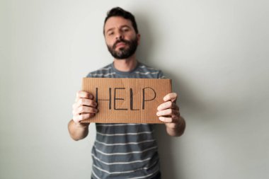 Depresyon ve kaygı içindeki İspanyol genç adam üzerinde yardım yazan bir tabela tutuyor. Depresyonda olan yetişkin bir adam destek ve tavsiye istiyor.