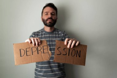 30 'larında İspanyol bir adam üstünde depresyon yazan bir tabelayı yırtıyor. Yetişkin adam depresyon sorununu aşıyor.