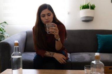 Kanepede tek başına oturan, içki içen ve depresyonda olan üzgün, genç bir kadın. 