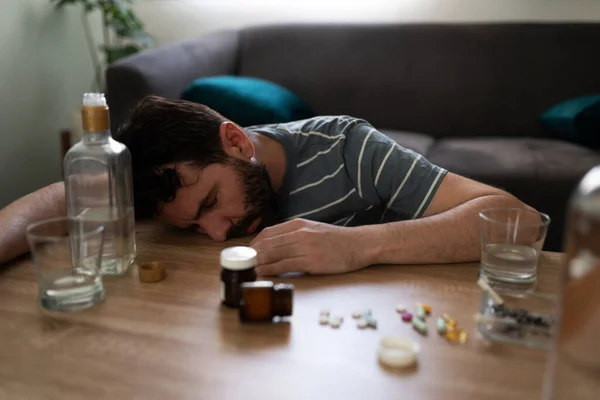 処方薬とアルコールのボトルで囲まれたテーブルの上に酔ったヒスパニック系の男が渡されます — ストック写真