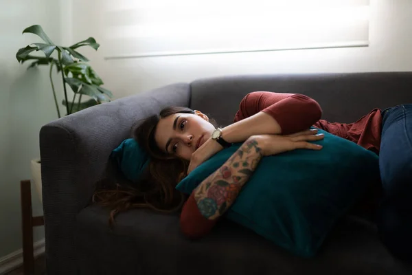 여성이 소파에 누워서 베개를 껴안고 있습니다 여자가 슬프고 보이네요 — 스톡 사진