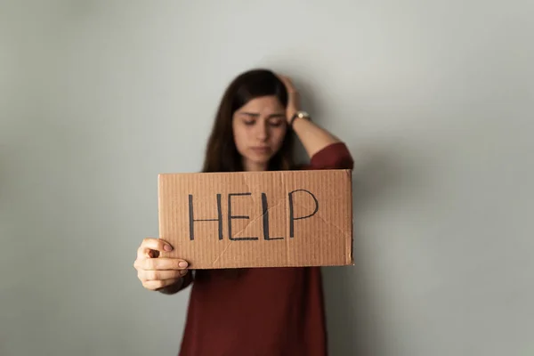 Hispanic young woman with depression and anxiety holding a sign with help written on it. Depressed woman asking for support and advice