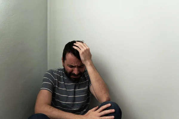 Sad hispanic man crying, sobbing and having an emotional breakdown in the floor. Adult man sitting alone in a house corner