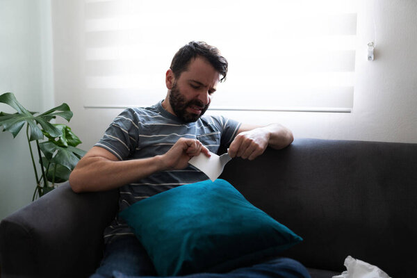 Взрослый латиноамериканец выглядит расстроенным и разбивает фотографию. Злобный мужчина 30 лет сидит в одиночестве на диване