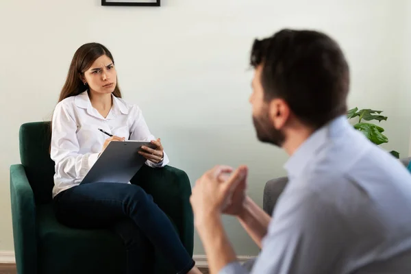 Female psychologist listening and paying attention to her male patient during a therapy session. Adult man with a lot of stress and problems talking about his issues