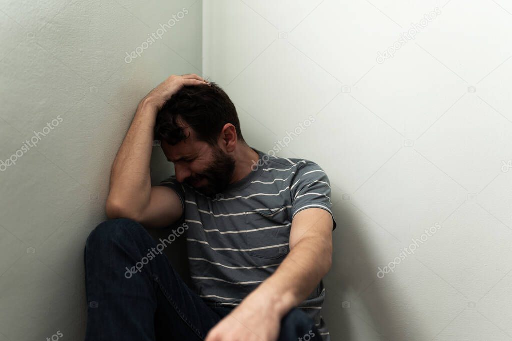 Sad adult man crying and suffering from psychological problems and solitude. Depressed man touching his hair and sitting on the floor
