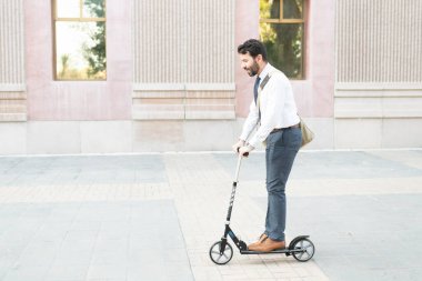 Latin yetişkin bir adam iş yerinin dışında scooter kullanıyor. 30 'lu yaşlarda bir adam işe gitmek için yeşil bir araç kullanıyor.