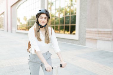 30 'lu yaşlarda, çevre dostu bir scooter ve şehir binasının dışında kaskla gezen mutlu bir kadın işçi. 