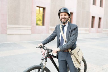 30 'lu yaşlarındaki mutlu Latin adam takım elbise ve kask giyiyor. İş yerine bisikletle giden bir işçi. 
