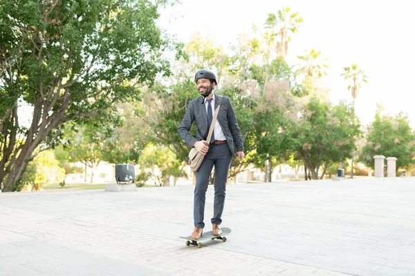 仕事から家までスケートボードに乗って旅行する幸せなヒスパニック系のビジネスマン 通勤に緑の交通機関を利用しようとする大人の男 — ストック写真