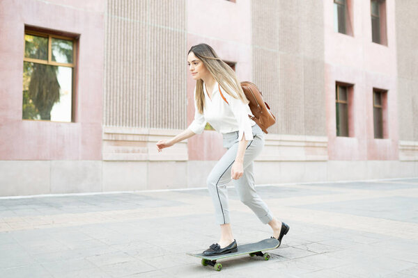 Professional woman with a backpack arriving to her work building in a skateboard 