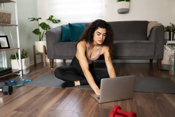 迷人的拉丁裔年轻女子在她的笔记本电脑中寻找一个视频锻炼 适合20多岁的女人坐在垫子上准备开始锻炼 — 图库照片