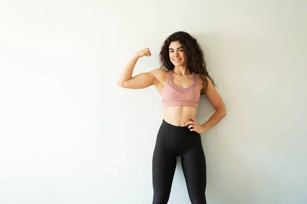 しっかりとした背景の前で彼女の強い腕を披露スポーツウェアを持つ筋肉ラテンの若い女性 スペースコンセプトのコピー — ストック写真
