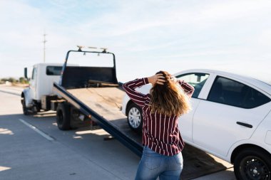 Üzgün genç bir sarışının, arabasının yol kenarındaki bir çekiciye çekilmesini izlemesi.