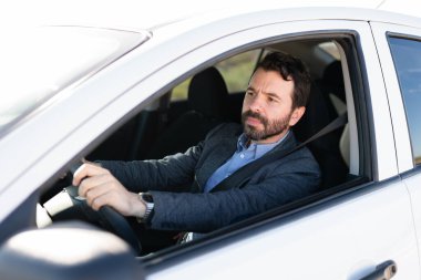 Erkek sürücü ileriye bakıyor ve otoyolda araba sürüyor. Kemerli ve elleri direksiyonda olan Latin bir adam. 