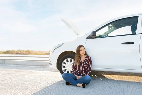 悲しい若い女性はフードを開いて 道路支援の助けを待っていると彼の壊れた車の横に道路に座って — ストック写真