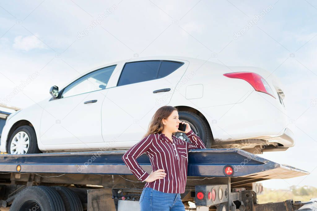 Side view of a young woman calling on the phone to ask for a ride because her car broke down on the highway and is being towed on a tow truck