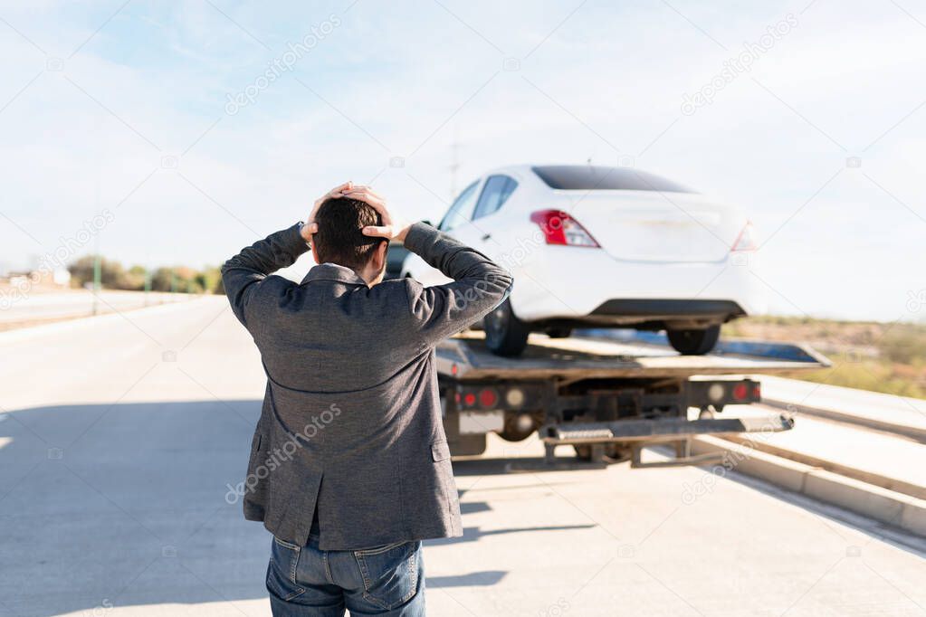 Rear view of a latin man looking annoyed with the hands in the head because they are taking his car in a tow truck