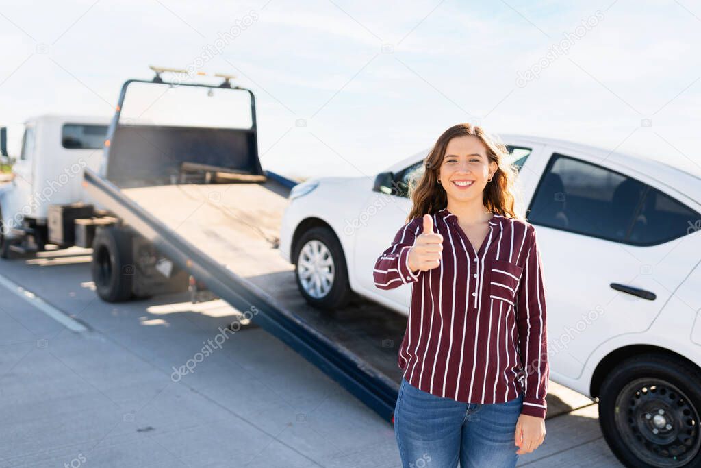 Caucasian woman in her 20s smiling and making a thumbs up sign. Young woman happy for the good and fast tow truck service she recieved for her broke-down car