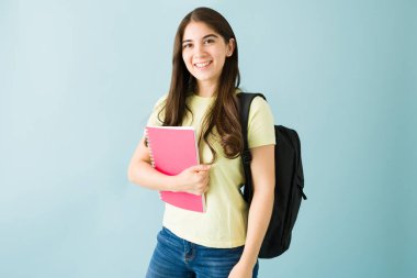 Not defteri ve sırt çantası taşıyan genç bir öğrencinin portresi. Güzel bir kadın mavi arka planda kameraya gülümsüyor.