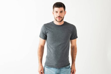 Yakışıklı, latin bir adamın günlük kıyafetler giyip beyaz bir arka planın önünde dikilirken çekilmiş bir fotoğraf.