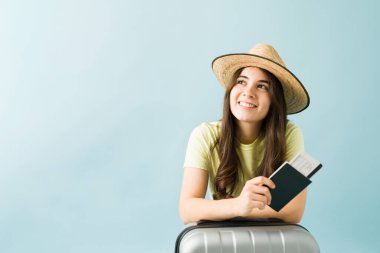 20 'li yaşlarda şapkalı güzel bir kadın seyahatinin hayalini kuruyor ve seyahat etmeye hazır. Pasaportu, uçak bileti ve bavulu olan bir kadın.