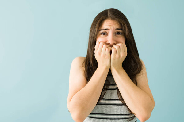 Stressed beautiful young woman looking scared and terrified biting her nails in front of a blue background