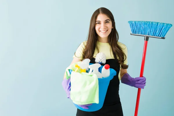 快乐的高加索女人拿着扫帚 提着装有清洁用品的水桶 拿着围裙和手套的年轻女人正要开始给她的房子消毒 — 图库照片