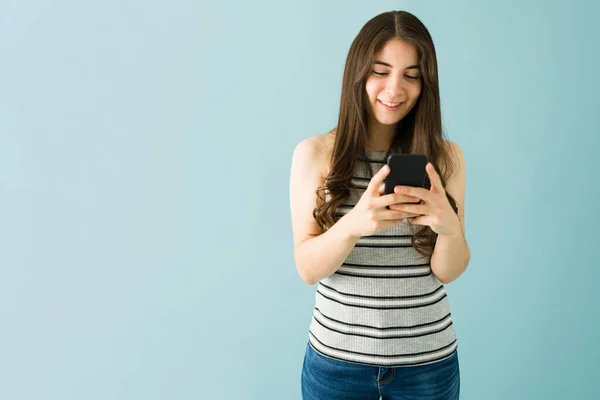 迷人的年轻女子面带微笑 在蓝色背景面前用手机发短信 — 图库照片
