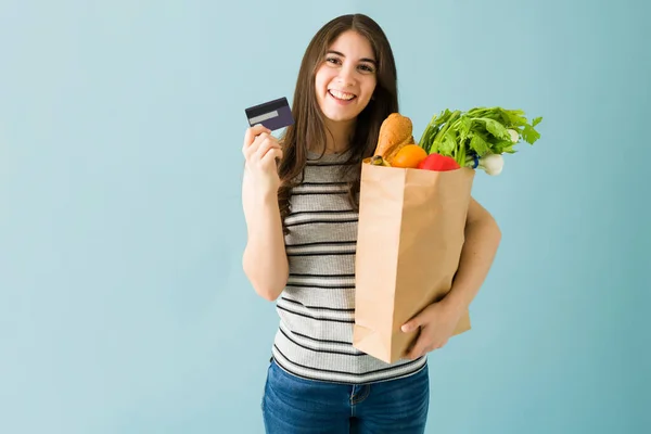 美しく 幸せな若い女性は彼女のクレジットカードで彼女の食料品のために支払った 青い背景に隔離された笑顔の女性 — ストック写真