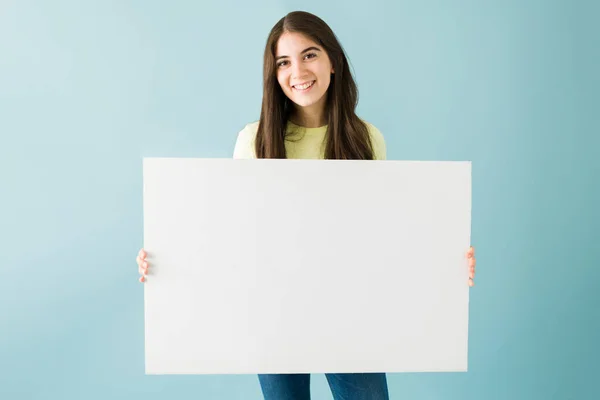 青い背景に白い空の看板を持ちながら笑顔と幸せそうに見える白人の若い女性の肖像画 — ストック写真
