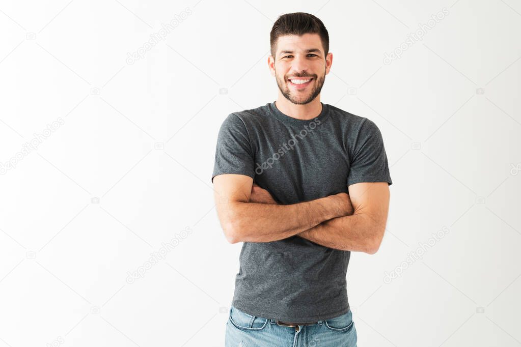 Happy hispanic young guy with his arms crossed and smiling in front of a white background